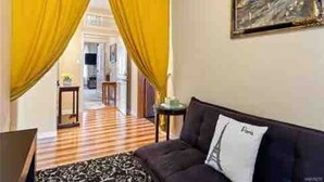 Une chambre d’hôtel avec un sol à carreaux, un canapé sombre agrémenté d’un coussin et des rideaux jaunes.