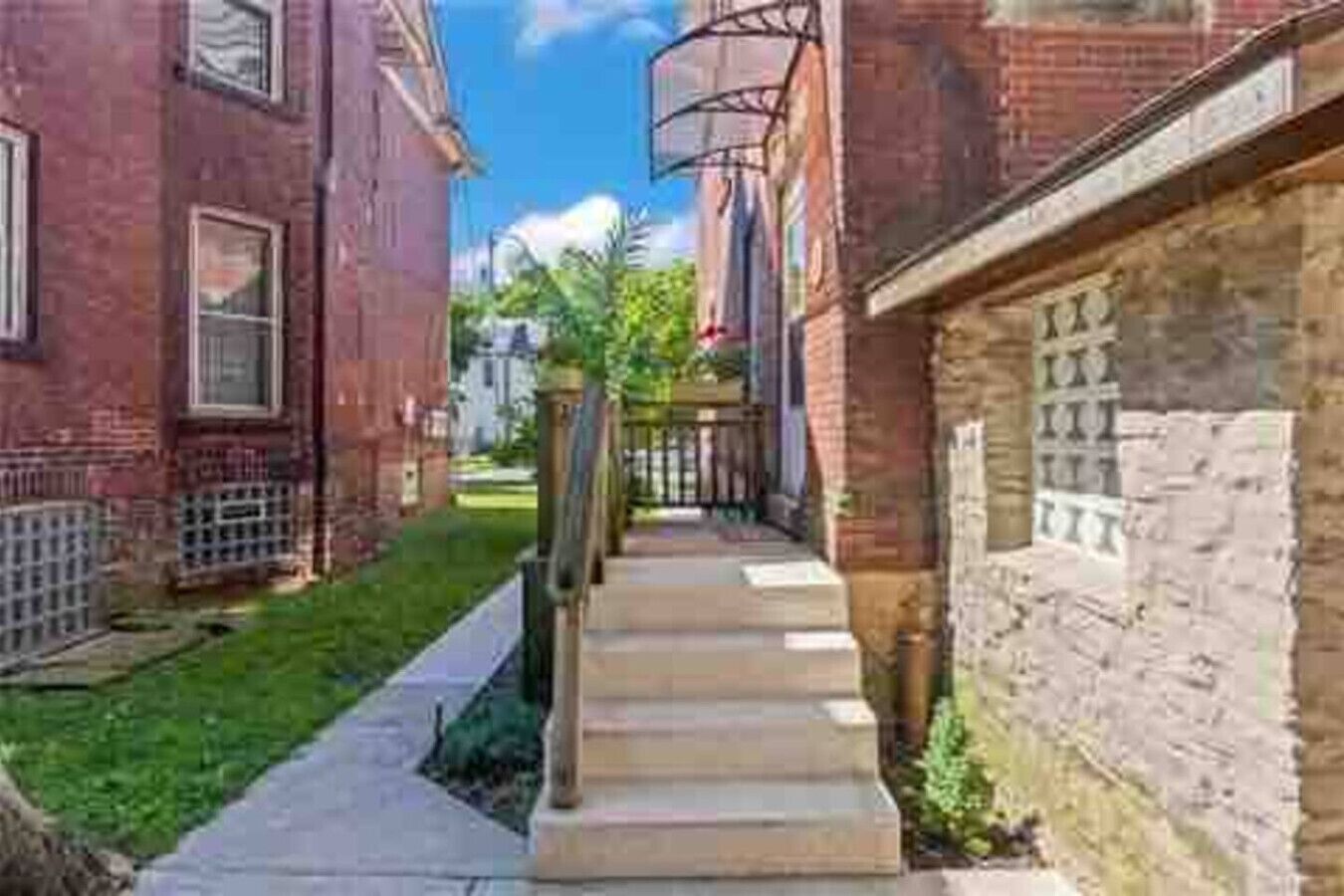A narrow alleyway with brick buildings on either side, a concrete pathway, and a metal fence.