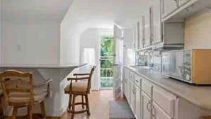 Une cuisine avec des meubles blancs, une chaise en bois et une vue sur l’extérieur.
