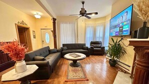 Un salon comprenant un ensemble de canapés, une table basse, un téléviseur fixé au mur et un ventilateur de plafond.