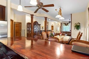 Un vaste espace dédié à la salle à manger, avec une longue table en bois, des chaises en cuir et un ventilateur de plafond.