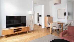 En moderne stue med et fladskærms-tv, et tv-møbel i træ og et spiseområde med bord og stole.