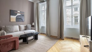 En moderne stue med sofa, sofabord og en rød lænestol. Der er et billede på væggen, en lampe og et vindue med gardiner.