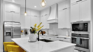A modern kitchen with white cabinetry, stainless steel appliances, and a central island with yellow chairs. - Luxe 4BR/3BA, 3 King Beds—Near AT&T, DFW, Dallas (Grand Prairie)