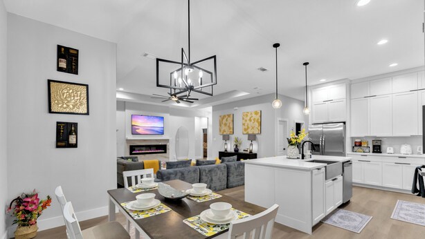 A modern kitchen with white cabinetry, a central island, and a dining area with a table set for four. - Luxe 4BR/3BA, 3 King Beds—Near AT&T, DFW, Dallas (Grand Prairie)