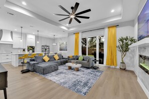 A modern living room with a sectional sofa, a coffee table, and a ceiling fan. - Luxe 4BR/3BA, 3 King Beds—Near AT&T, DFW, Dallas (Grand Prairie)