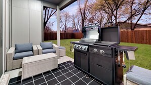 A covered patio with a grill, outdoor furniture, and a view of a backyard. - Luxe 4BR/3BA, 3 King Beds—Near AT&T, DFW, Dallas (Grand Prairie)