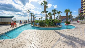 A swimming pool area with palm trees, a poolside bar, and a building with balconies. - Nana's Sweet Retreat at Ocean Walk (Daytona Beach)