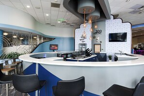 A modern reception area with a curved counter, black chairs, and a patterned wall. - Nana's Sweet Retreat at Ocean Walk (Daytona Beach)