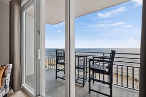 A balcony with a view of the beach, a table, and two chairs. - Nana's Sweet Retreat at Ocean Walk (Daytona Beach)