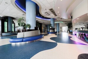 A spacious lobby with a curved seating area, large pillars, and potted plants. - Nana's Sweet Retreat at Ocean Walk (Daytona Beach)