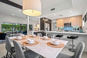A modern kitchen with a large island, built-in appliances, and a dining area with a marble table and grey chairs. - Poolside Paradise in Palm Springs - Your Private Palm Springs Oasis: Pool, Spa & Stunning Views (Palm Springs)
