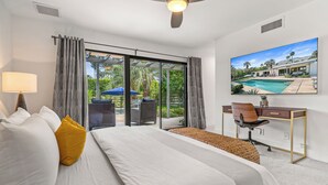 Ein Hotelzimmer mit Bett, Schreibtisch, Stuhl und einem großen Fenster mit Blick auf einen Pool und Grünflächen.