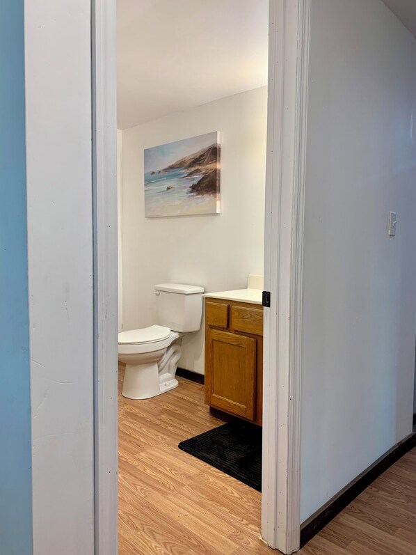 Une salle de bain avec des toilettes blanches, des meubles en bois et un tableau représentant une scène de plage au mur.