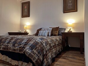 A bedroom with a plaid bedspread, two bedside lamps, and framed artwork on the walls. - Cozy 3BR Home, Patio + Firepit, Sleeps 6 (Athens)