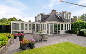 Ett modernt hus med ett stort glashus, en uteplats och en välskött trädgård.