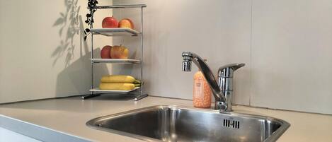 A kitchen with a stainless steel sink, a fruit shelf, and a hand soap dispenser.