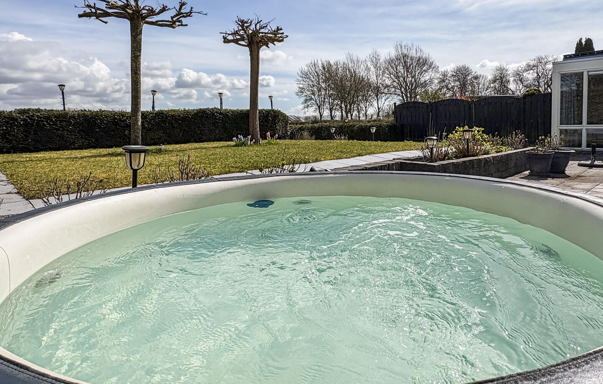 A swimming pool with a clear water surface, surrounded by a landscaped garden with hedges and trees.