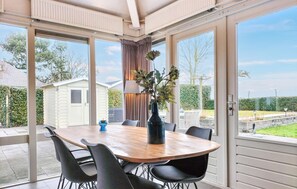 A conservatory with a wooden table and black chairs, large windows, and a view of a garden. - Nice home in Stavenisse with swimming pool (Stavenisse)