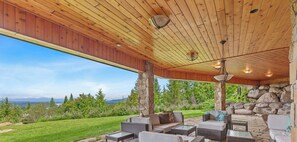 A covered patio with stone walls, outdoor furniture, and a view of a mountainous landscape. - NW Tuscan Retreat — 180° Vistas & Private Hot Tub (Harrison)