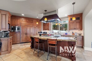 A kitchen with wooden cabinets, a built-in microwave, a gas stove, and a large island with bar stools. - NW Tuscan Retreat — 180° Vistas & Private Hot Tub (Harrison)
