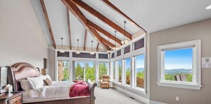 A bedroom with a large window, a bed, and a chair. - NW Tuscan Retreat — 180° Vistas & Private Hot Tub (Harrison)