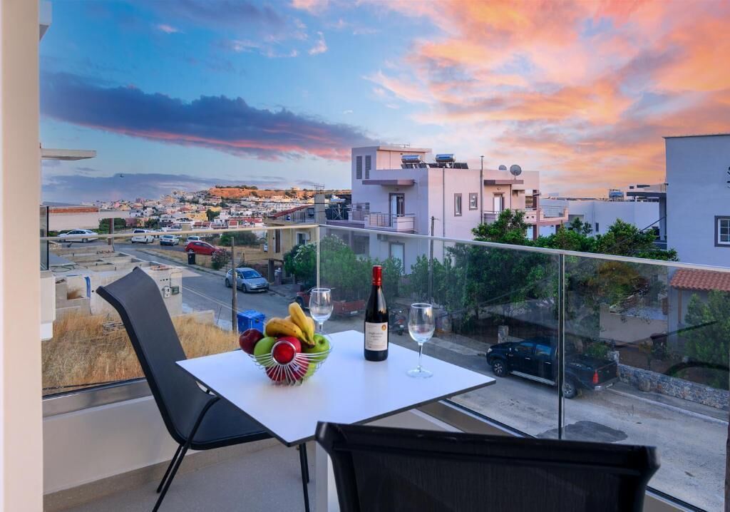 A balcony with a table set for two, a bottle of wine, and a bowl of fruit.