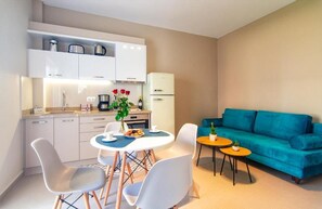 En kompakt bolig med tekøkken, spiseplads og en teal farvet sofa.