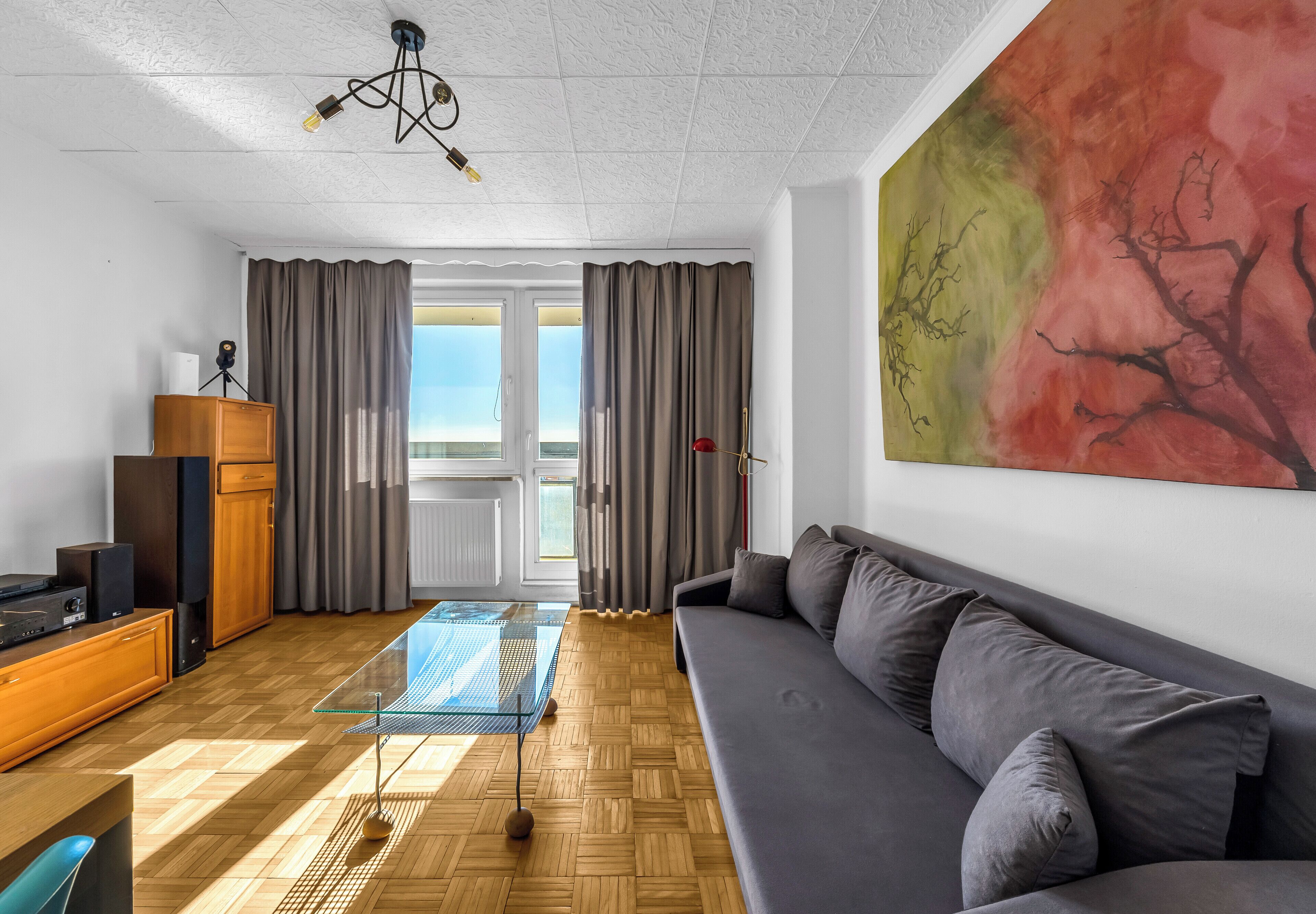 Ein modernes Wohnzimmer mit einer Couch, einem Glastisch, einem Holzschrank und einem großen abstrakten Gemälde.