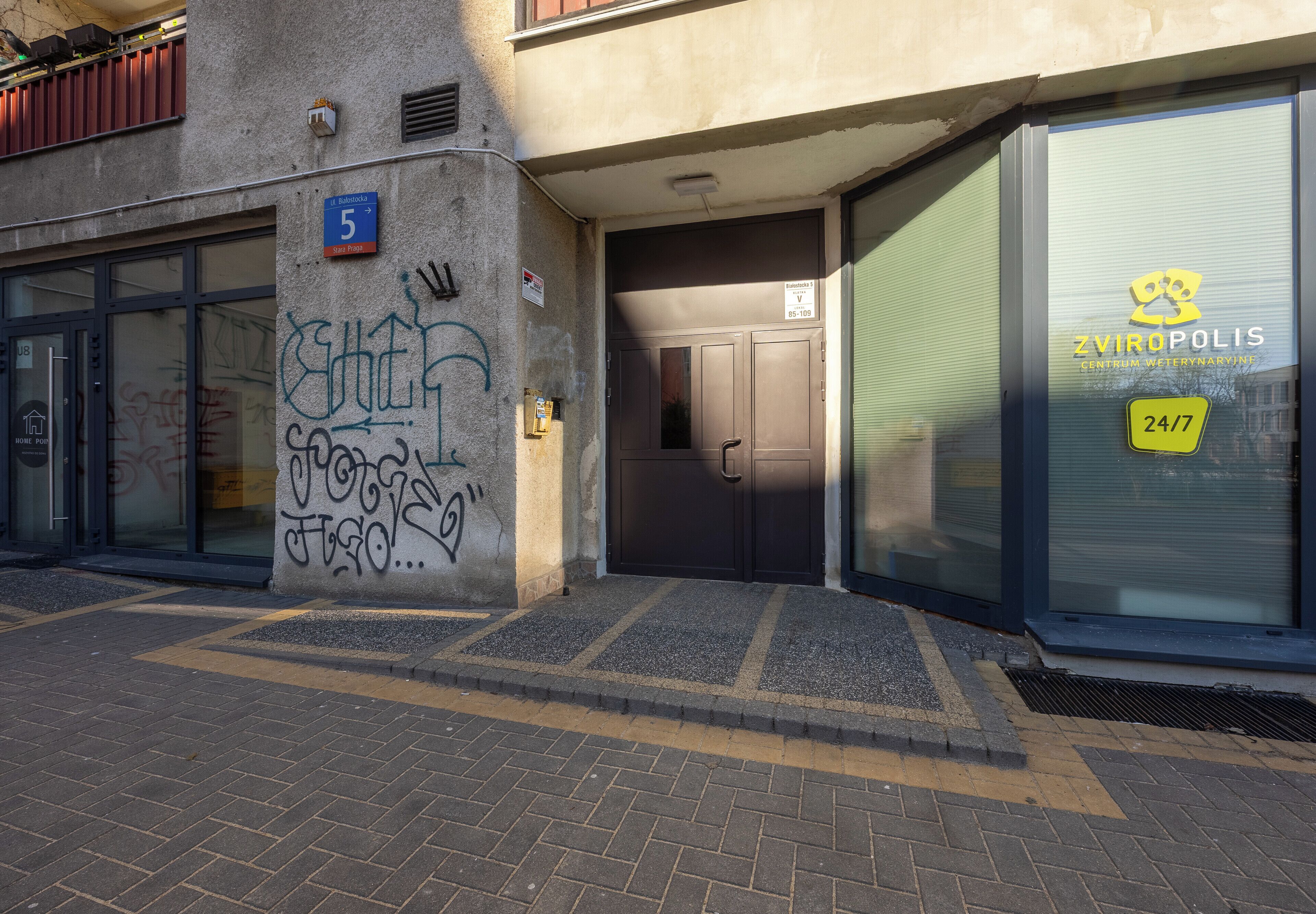 Ein Gebäude mit einer geschlossenen Tür, einem sichtbaren Hinweisschild mit der Nummer 5 und einem Schild mit der Aufschrift '24/7' am Fenster.