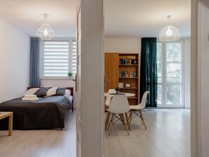 A bedroom with a bed, bedside table, and a window with blinds. - Toruń Urban Comfort Apartment (Toruń)