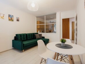 Un espacio habitable moderno con un sofá verde, una mesa de comedor redonda y una ventana con vistas a una cocina.