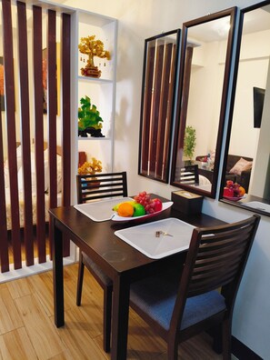 Un coin repas avec une table en bois, des chaises, un panier de fruits et une étagère décorative.