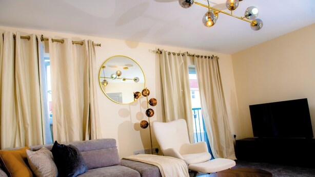 Una sala de estar con sofá, sillón, mesa de centro, televisor y un espejo con lámpara.