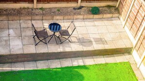 Un patio con una mesa y sillas, una pequeña mesa redonda y un área de césped verde.