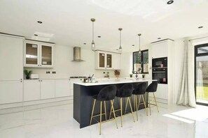Una cocina moderna con armarios blancos, una isla negra con taburetes altos e iluminación colgante.