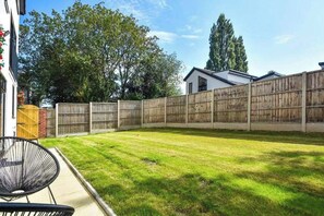 A backyard with a wooden fence, a lawn, and a house in the background.