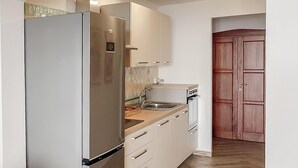 A compact kitchen with a stainless steel refrigerator, white cabinets, a wooden countertop, and a built-in sink.