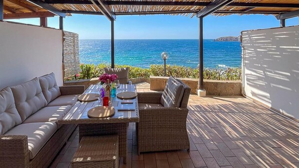 An outdoor patio with wicker furniture, a table set for dining, and a view of the ocean.