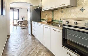 A kitchen with white cabinets, a wooden herringbone floor, a built-in oven, and a tiled backsplash.
