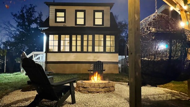 A two-story house with a fire pit in the front yard, a swing set, and a pergola with string lights. - Relaxing 3-bedroom house in terrific Cincinnati with Firepit and Patio (Cincinnati)