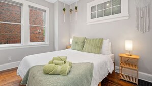 A neatly arranged bedroom with a large bed, a bedside table with a lamp, and a view of a brick wall through a window. - Relaxing 3-bedroom house in terrific Cincinnati with Firepit and Patio (Cincinnati)