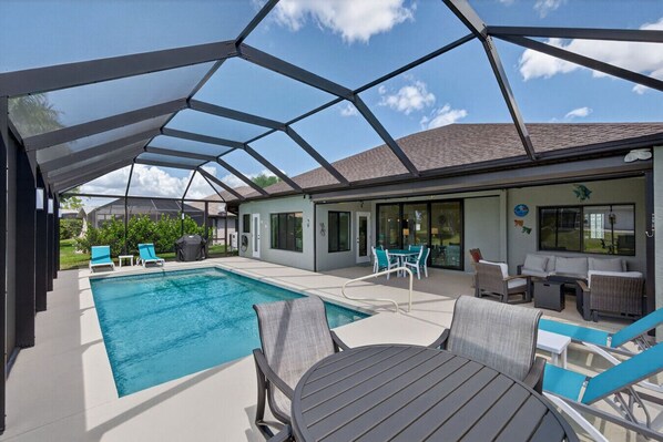 A covered outdoor swimming pool with lounge chairs and a table, surrounded by a house with a patio and a covered area. - Sunset Retreat with heated pool (Rotonda West)
