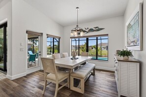 A dining area with a large table, chairs, and a bench. There is a view of a swimming pool and greenery outside. - Sunset Retreat with heated pool (Rotonda West)