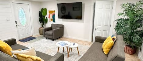 Un salon moderne avec deux canapés gris, une table basse et un téléviseur fixé au mur au-dessus d’un des canapés gris.