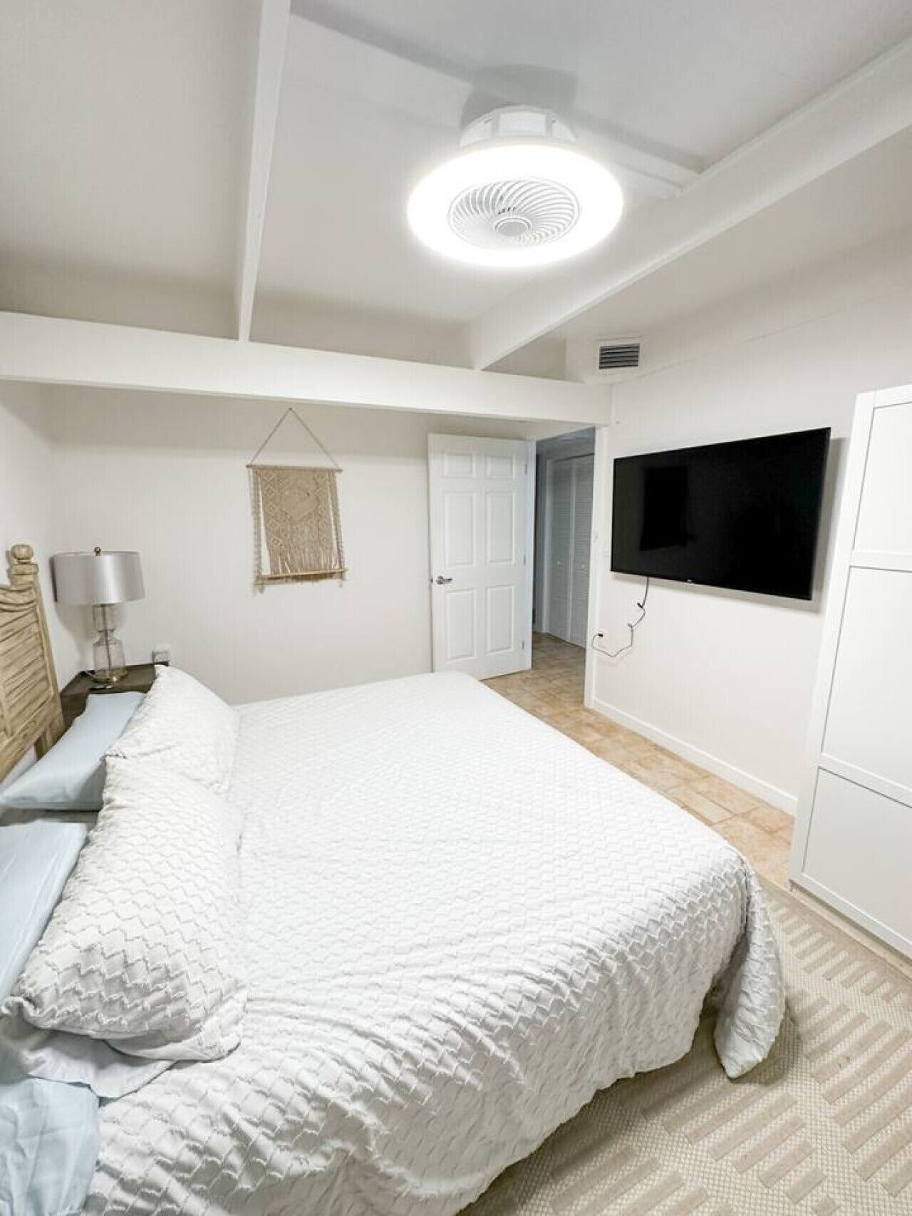 Un dormitorio con una cama grande, un televisor montado en la pared y una lámpara en el techo.