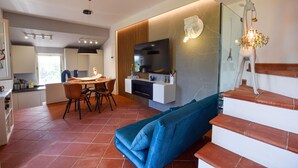 Una sala de estar moderna con un sofá azul, un televisor montado en una pared de paneles de madera y una escalera decorada con una figura de jirafa.