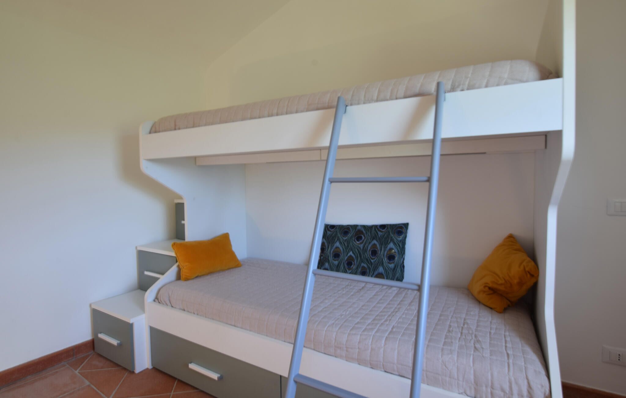 A bunk bed with a ladder, two pillows, a small desk, and a drawer unit.