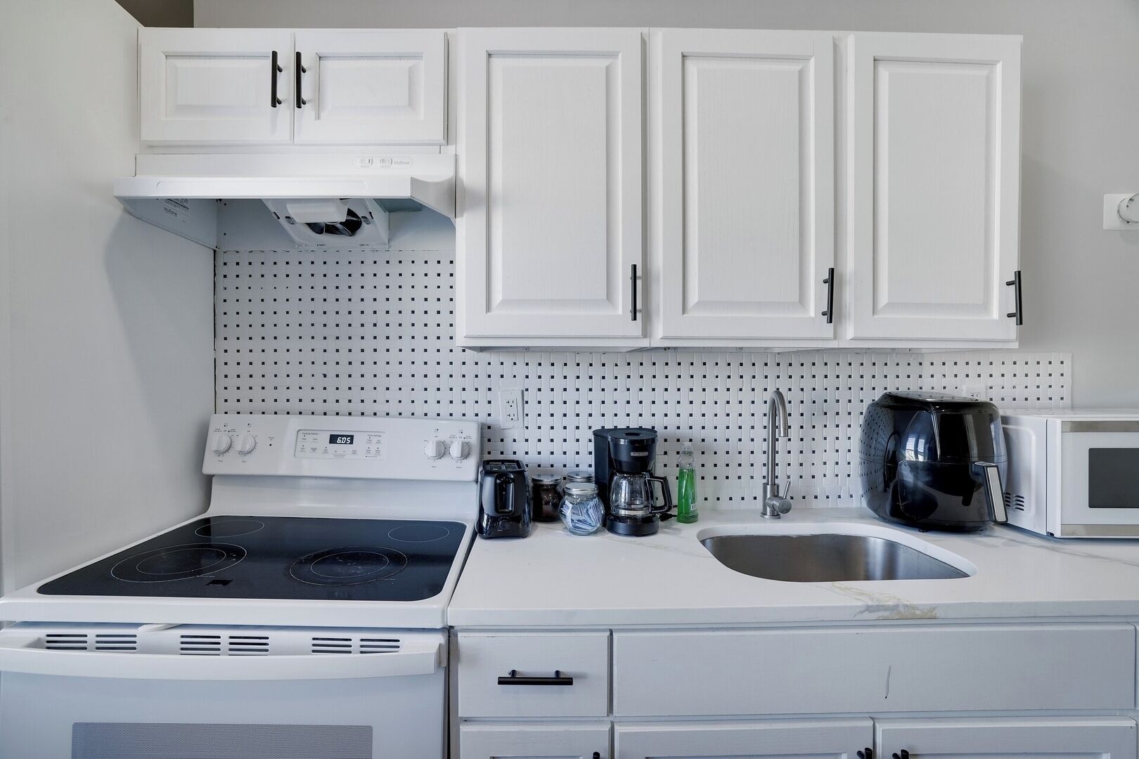 A kitchen with white cabinets, a stove, a microwave, a coffee maker, and a sink.