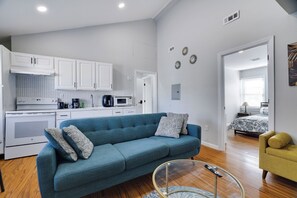 Eine moderne Küche mit weißen Schränken, einem blauen Sofa mit gemusterten Kissen und einem gelben Sessel.
